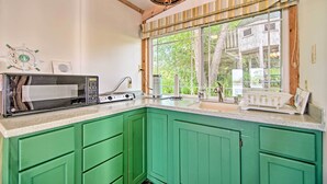 A kitchen with green cabinets, a microwave, a coffee maker, and a window with a view of a tree and a wooden structure. - Rock River Access! Peaceful Horicon Studio (Horicon)