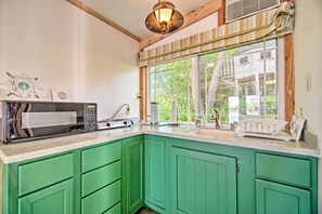 A kitchen with green cabinets, a microwave, a coffee maker, and a window with a view of a tree and a wooden structure. - Rock River Access! Peaceful Horicon Studio (Horicon)