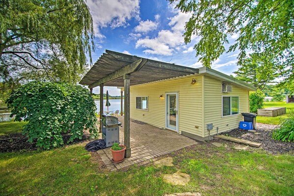 A small, single-story house with a covered patio, a grill, and a view of a lake.