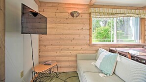 A cozy cabin interior with a wooden wall, a cushioned bench, a table, and a window with a view of greenery. - Rock River Access! Peaceful Horicon Studio (Horicon)