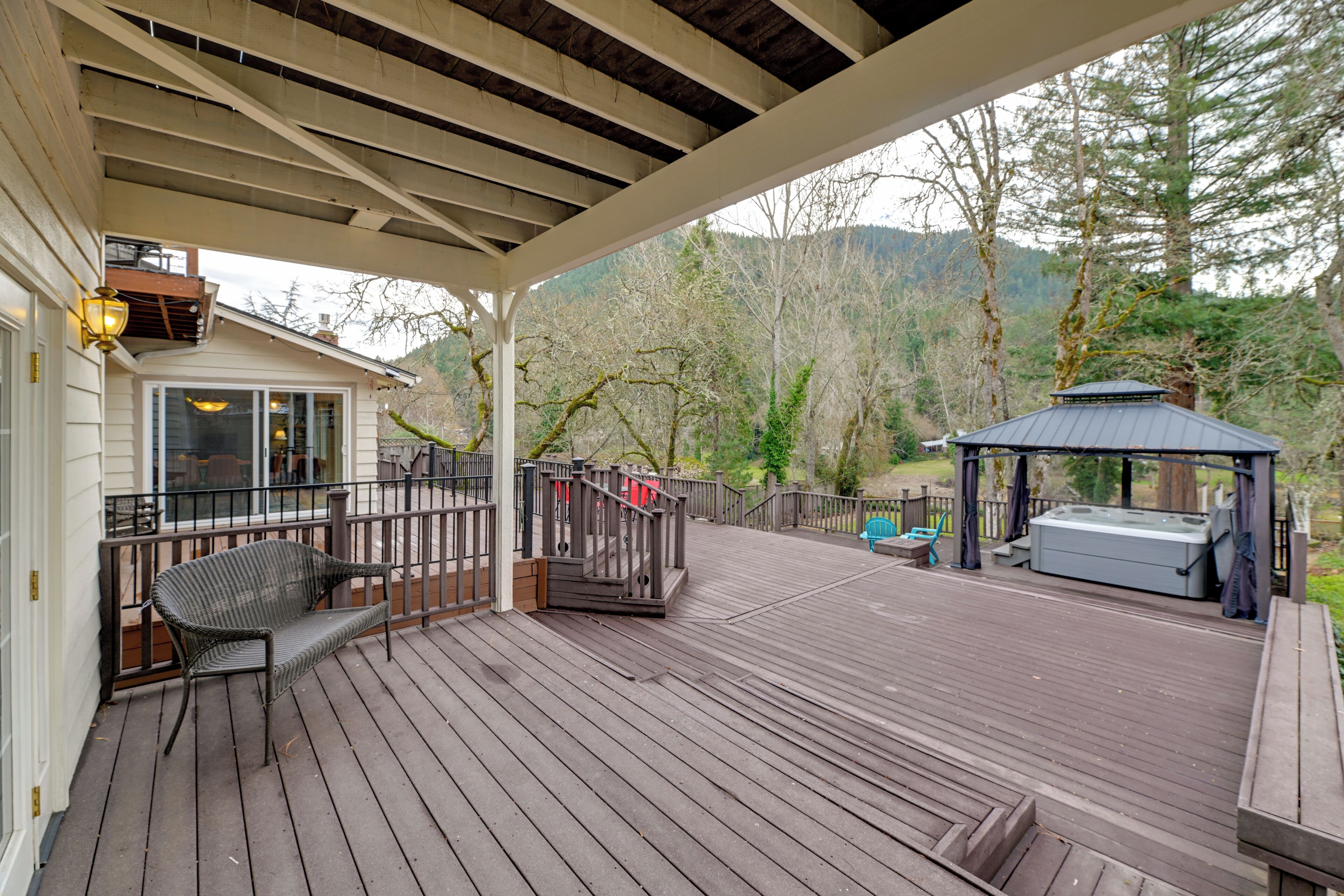 Un patio in legno con zona salotto coperta, vasca idromassaggio e gazebo.