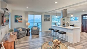 A modern living room with a large window, a kitchen island, and a seating area with a view of the ocean. - Tacoma 'dash Point Beach Cabin' w/ Balcony! (Tacoma)