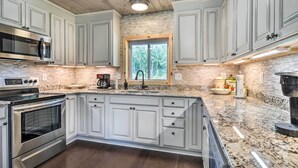 A kitchen with white cabinets, a granite countertop, a built-in oven, and a window with a view of trees.
