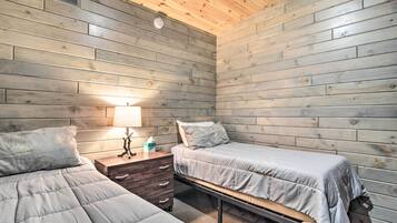 A room with two beds, a nightstand, a lamp, and a wooden ceiling.