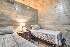 A room with two beds, a nightstand, a lamp, and a wooden ceiling.