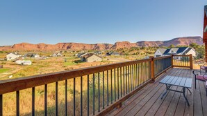 A wooden deck with a table and chairs, overlooking a residential area with houses and a mountainous landscape. - 'the Cliffrose Cabin' - Hike, Relax, Explore! (Kanab)