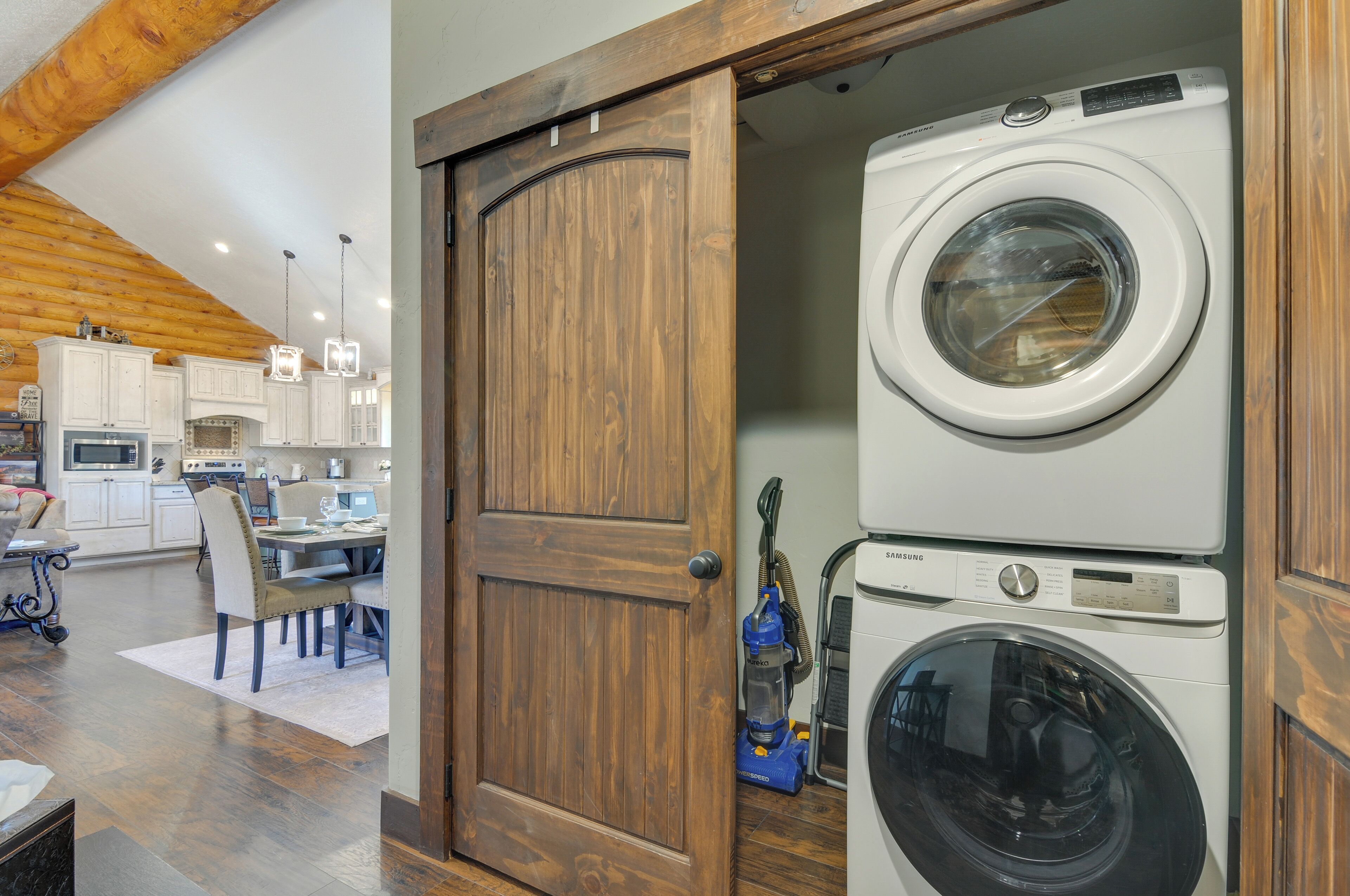 A laundry room with stacked washers and dryers, a wooden door, and a dining area with a table and chairs.