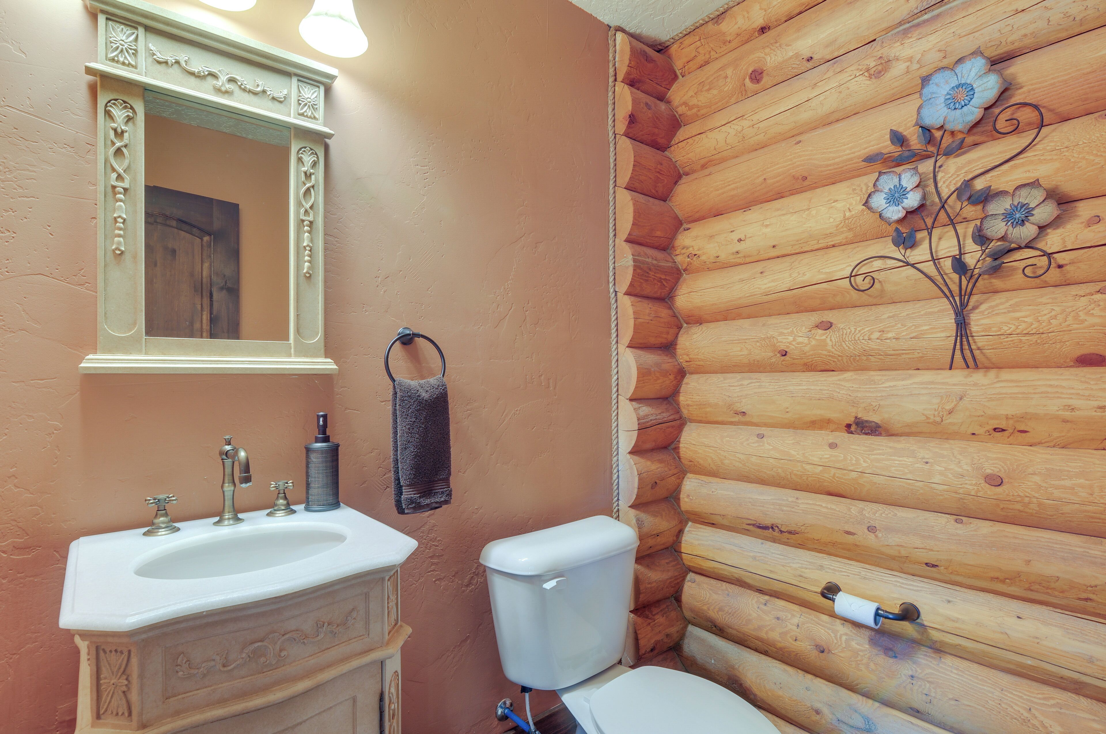 A bathroom with a wooden log wall, a white sink with a mirror, and a toilet.