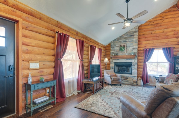 A log cabin interior with a fireplace, wooden walls, a ceiling fan, and a cozy seating area. - 'the Cliffrose Cabin' - Hike, Relax, Explore! (Kanab)