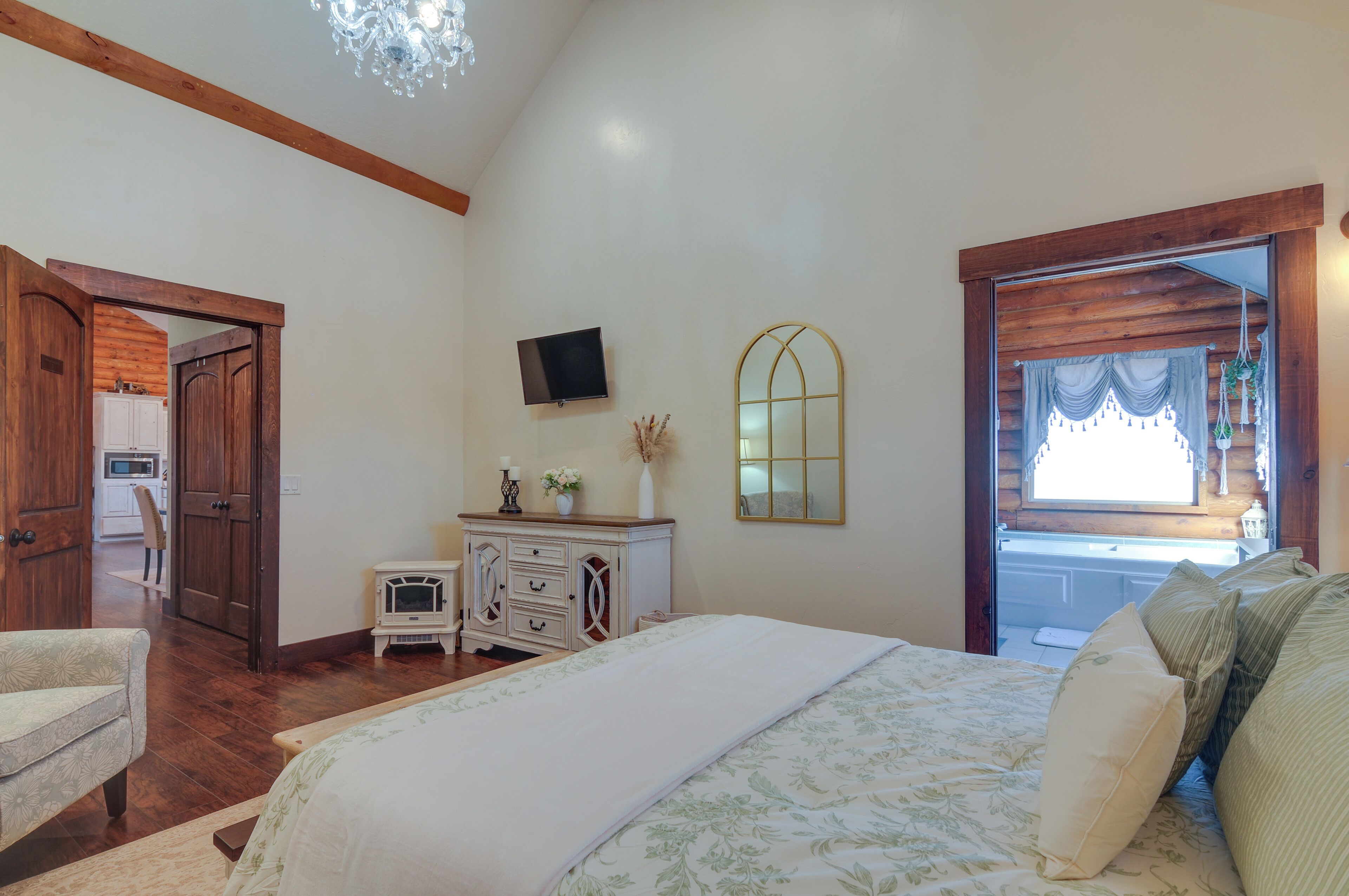 Une chambre à coucher avec un grand lit, une commode, un téléviseur et une fenêtre avec des rideaux.