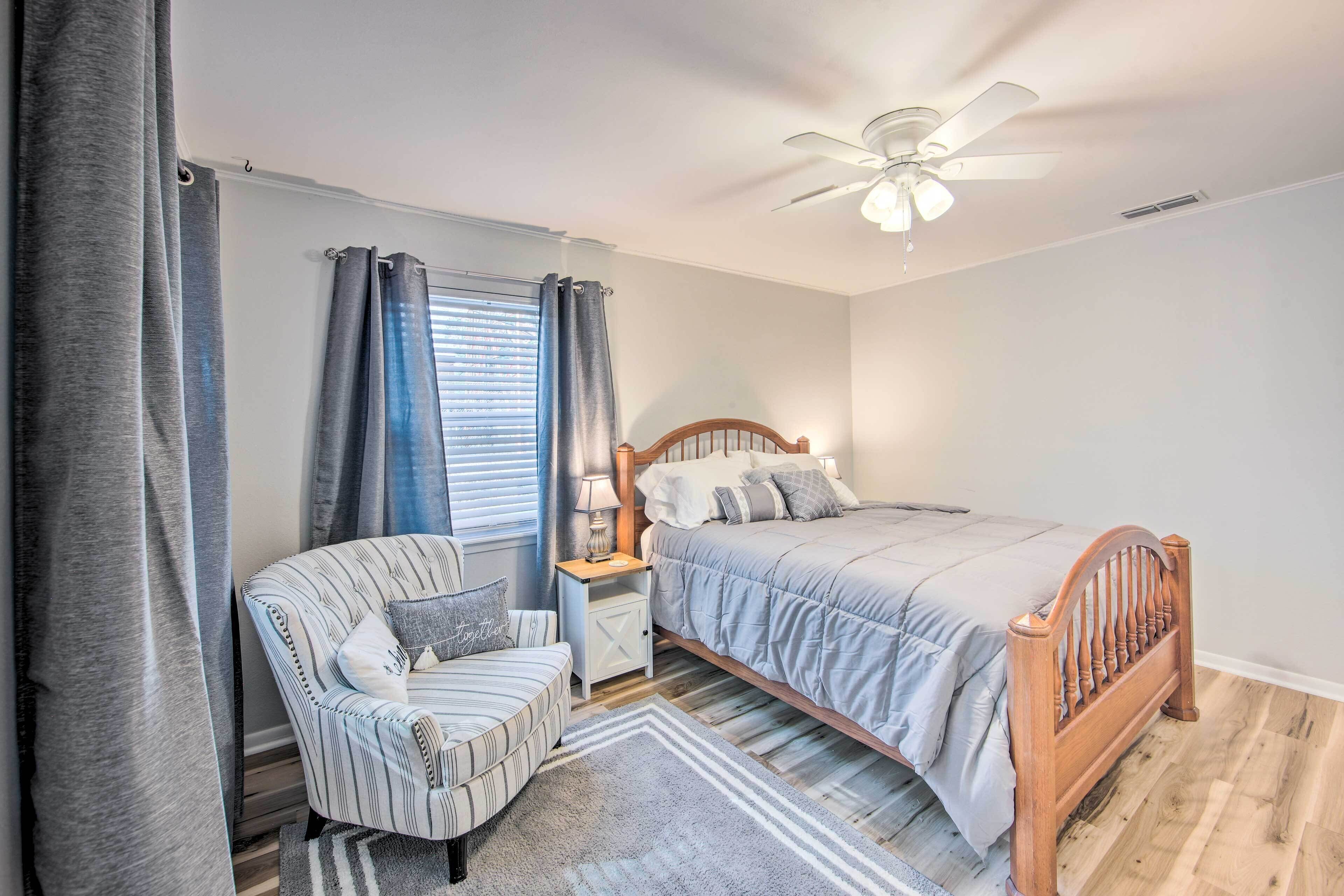 A bedroom with a bed, a chair, a nightstand, a ceiling fan, and a window with curtains.