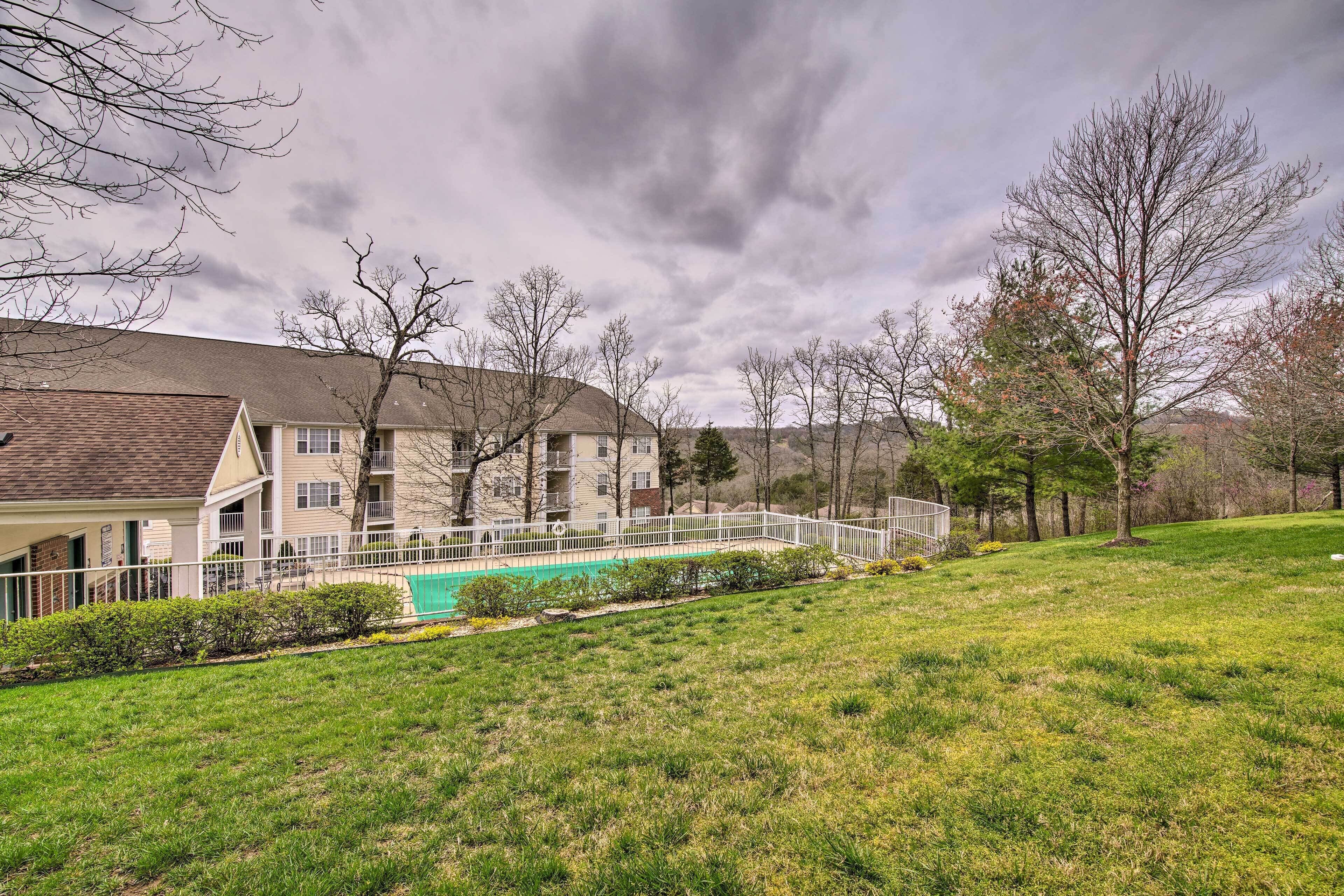 A residential area with a swimming pool, a white fence, and a grassy lawn.