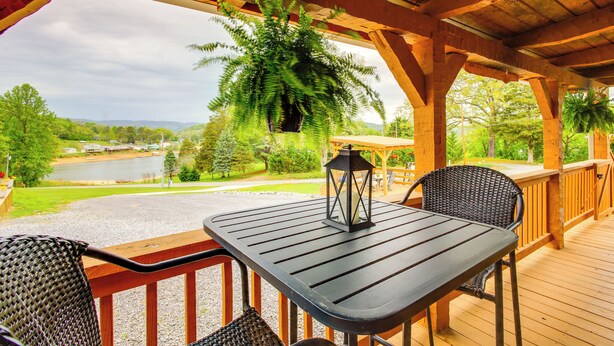 A wooden deck with a table and chairs, overlooking a lake and greenery. - Rivers View - Cherokee Lake Cabin w/ Fire Pit! (Bean Station)