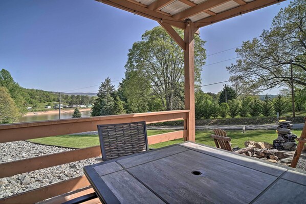 A wooden deck with a table and chairs overlooking a lake and forest.