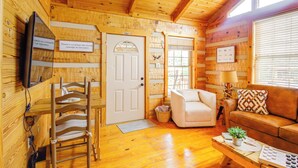 A cozy cabin interior with a wooden interior, a white door, a sofa, a chair, and a small table with a plant. - Rivers View - Cherokee Lake Cabin w/ Fire Pit! (Bean Station)
