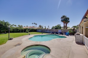A backyard with a swimming pool, a hot tub, and a patio area with lounge chairs.