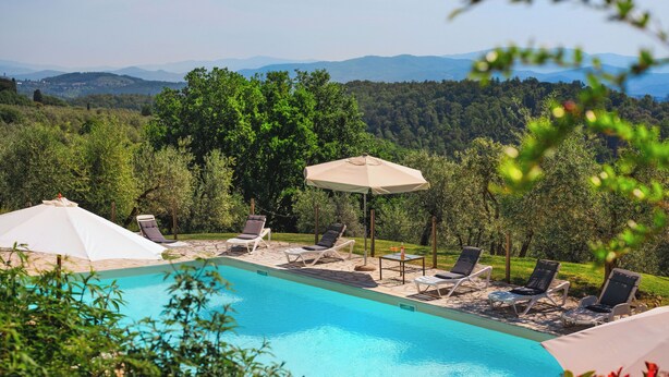 Ein Swimmingpool mit Liegestühlen und Sonnenschirmen, umgeben von üppiger Vegetation und Bergen im Hintergrund.