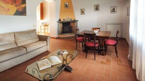 Ein gemütliches Wohnzimmer mit einer Couch, einem Glastisch mit offenem Buch, einem Kamin und einem Essbereich mit Stühlen und Tisch.
