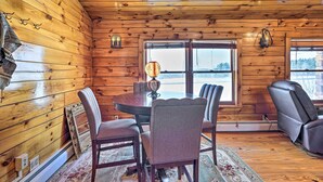 Interno di una baita in legno con tavolo da pranzo, sedie e camino.