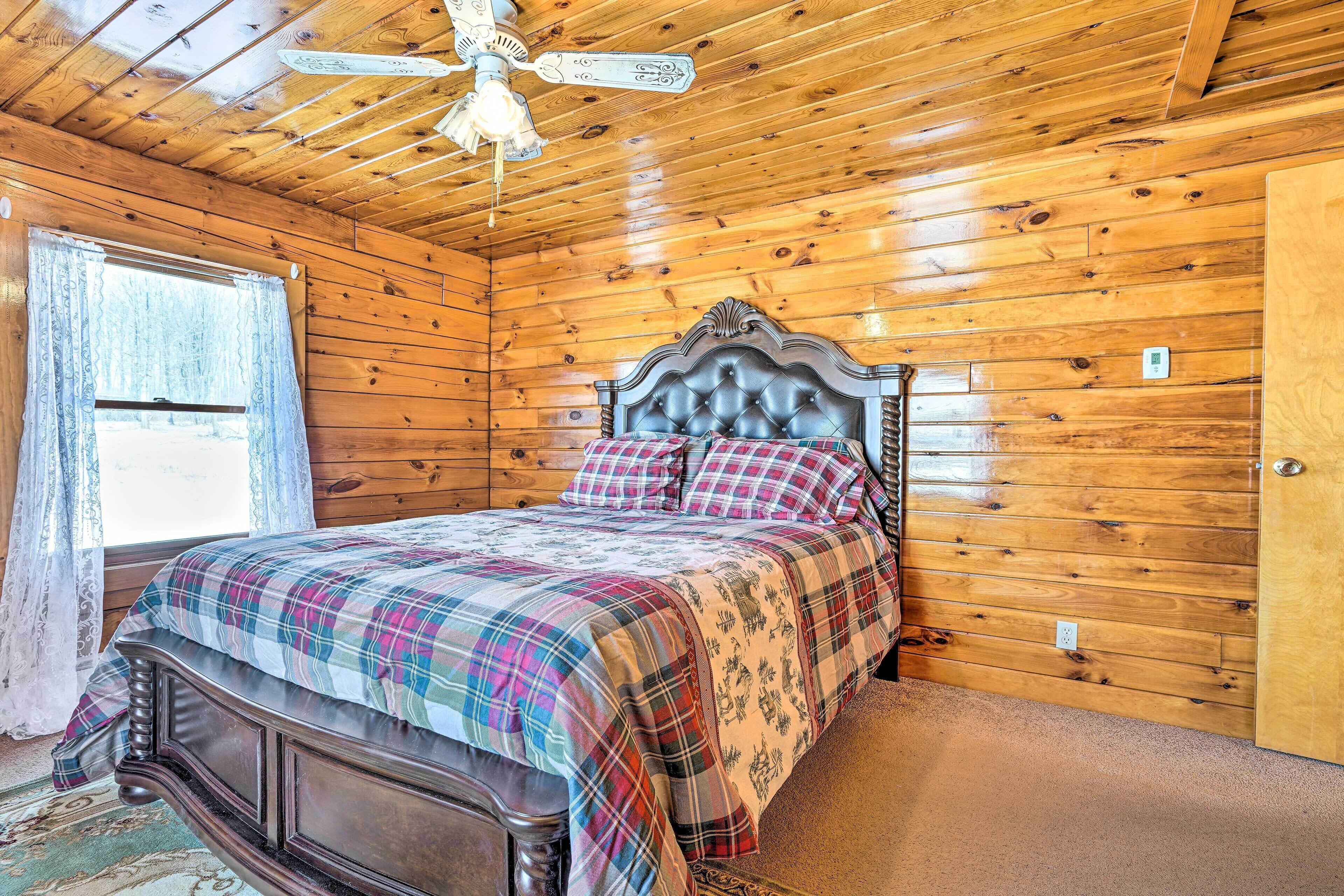 Ein Schlafzimmer einer Holzhütte mit Bett, Deckenventilator und einem Fenster mit Vorhängen.