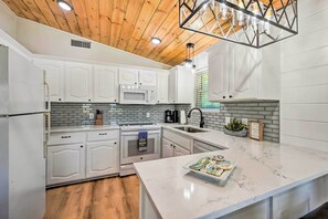 Une cuisine moderne avec des meubles blancs, un plan de travail en marbre et un plafond en bois.