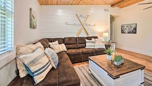 Un accogliente soggiorno con un divano ad angolo in pelle marrone, un tavolino in legno e una parete bianca con un'insegna che riporta la scritta 'Farmhouse Retreat'.