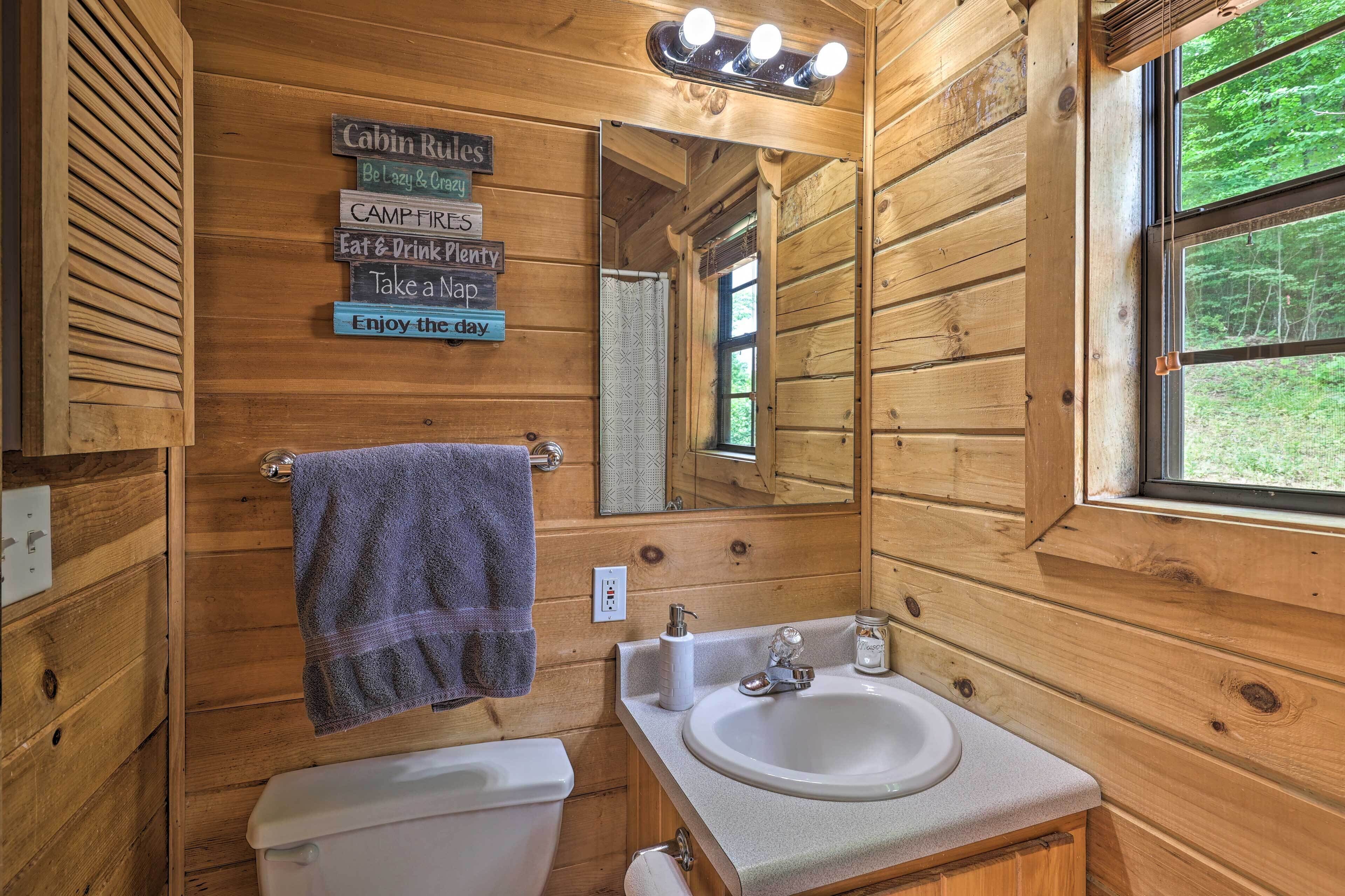 Une salle de bain rustique, aménagée dans une cabane en bois, avec un lavabo, des toilettes et une serviette accrochée au mur.
