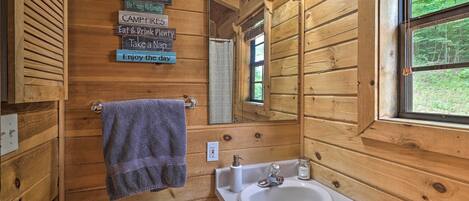 Une salle de bain rustique, aménagée dans une cabane en bois, avec un lavabo, des toilettes et une serviette accrochée au mur.