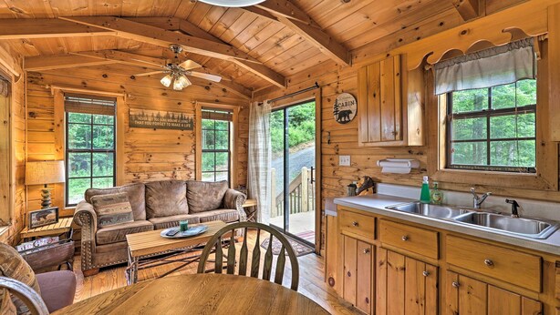 A cabin interior with a wooden dining table, a sofa, a kitchen with a sink, and a ceiling fan. - Quaint Log Cabin w/ Views Near West Jefferson (Warrensville)