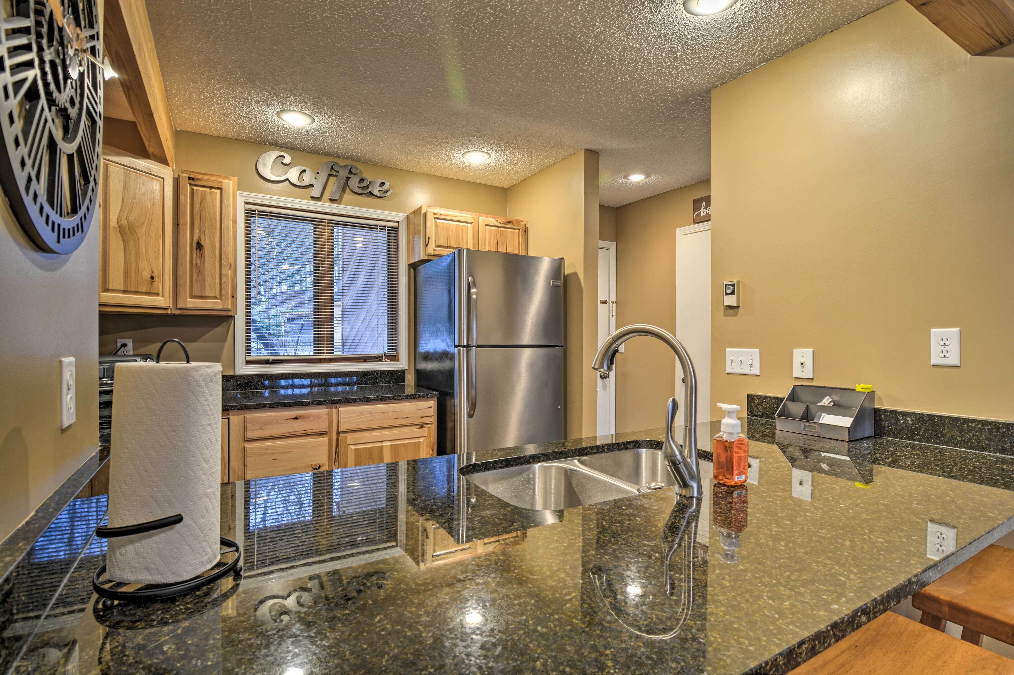 A kitchen with a stainless steel refrigerator, a sink, wooden cabinets, and a countertop with a paper towel dispenser.