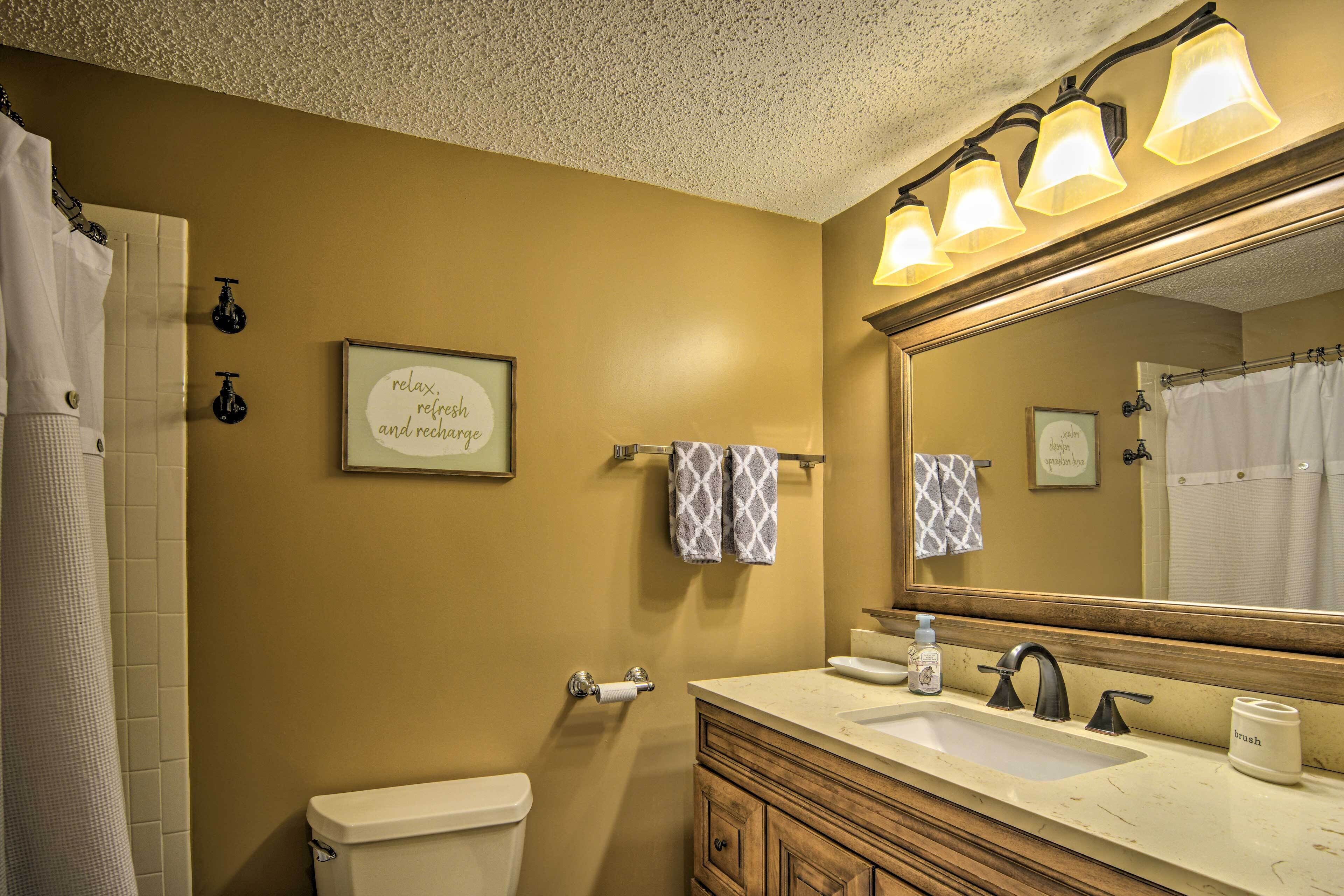 A bathroom with a beige wall, a wooden vanity, a sink, a mirror, and a toilet.