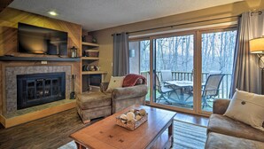 A cozy living room with a fireplace, a flat-screen TV mounted above it, and a comfortable seating area with a sofa and armchairs. - Cozy Bellaire Condo w/ Balcony - 3 Mi to Skiing! (Bellaire)