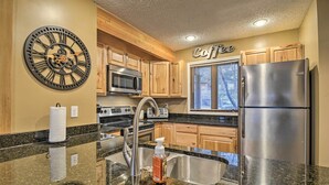 A kitchen with wooden cabinets, stainless steel appliances, a large clock, and a window with blinds. - Cozy Bellaire Condo w/ Balcony - 3 Mi to Skiing! (Bellaire)