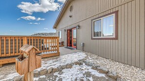 A wooden building with a red door and windows, a wooden deck, and a bird feeder. - Modern Mtn Home w/ Sports Court, Near Alto Lake! (Alto)
