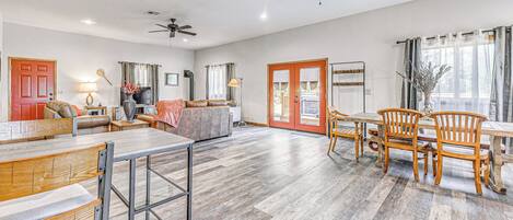 A spacious living area with a dining table, chairs, and a sofa. There are ceiling fans, a fireplace, and a view of the outdoors.