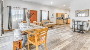 A spacious living area with a wooden dining table, chairs, a sofa, and a kitchen in the background. - Modern Mtn Home w/ Sports Court, Near Alto Lake! (Alto)