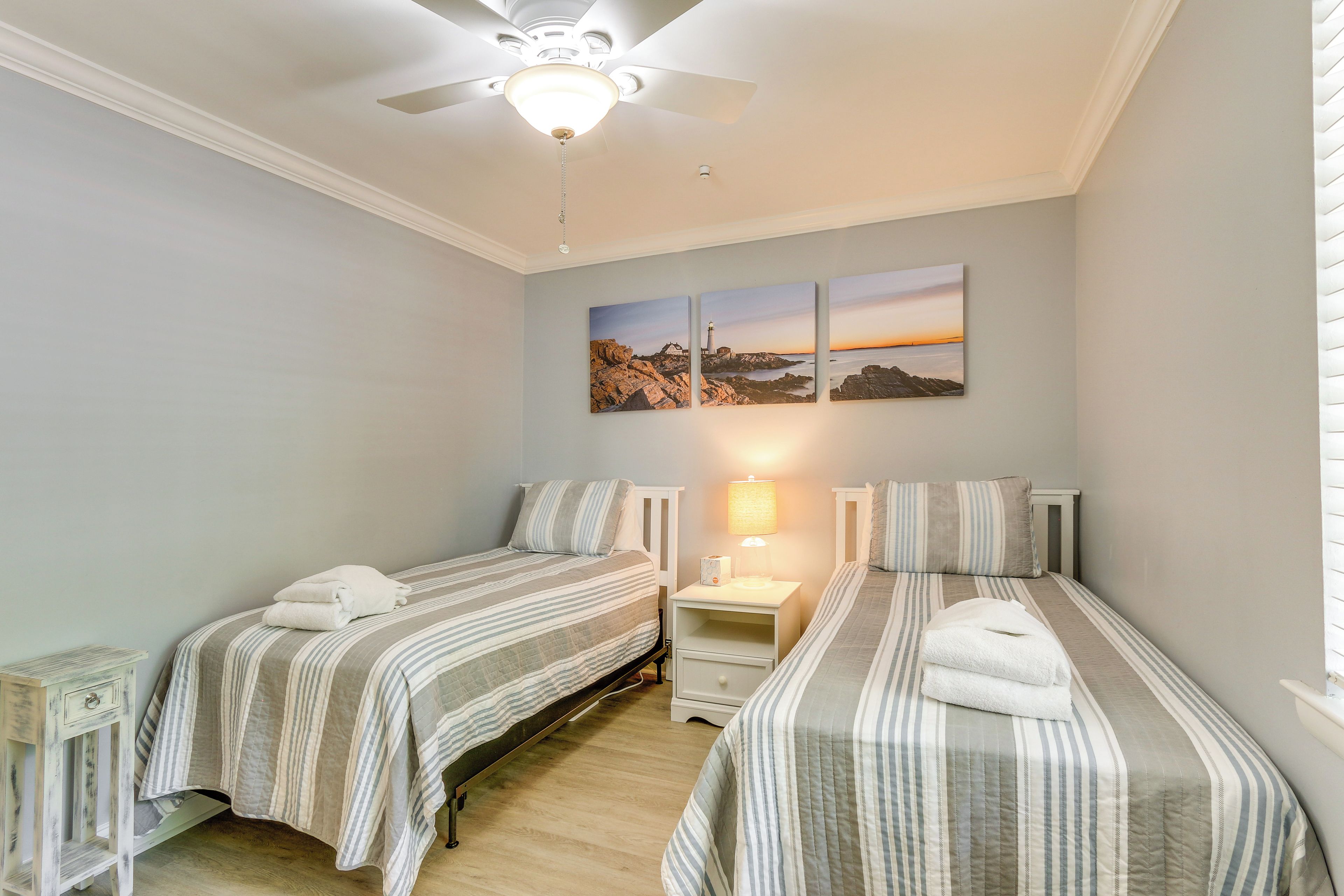 A bedroom with two beds, a ceiling fan, and a nightstand with a lamp.