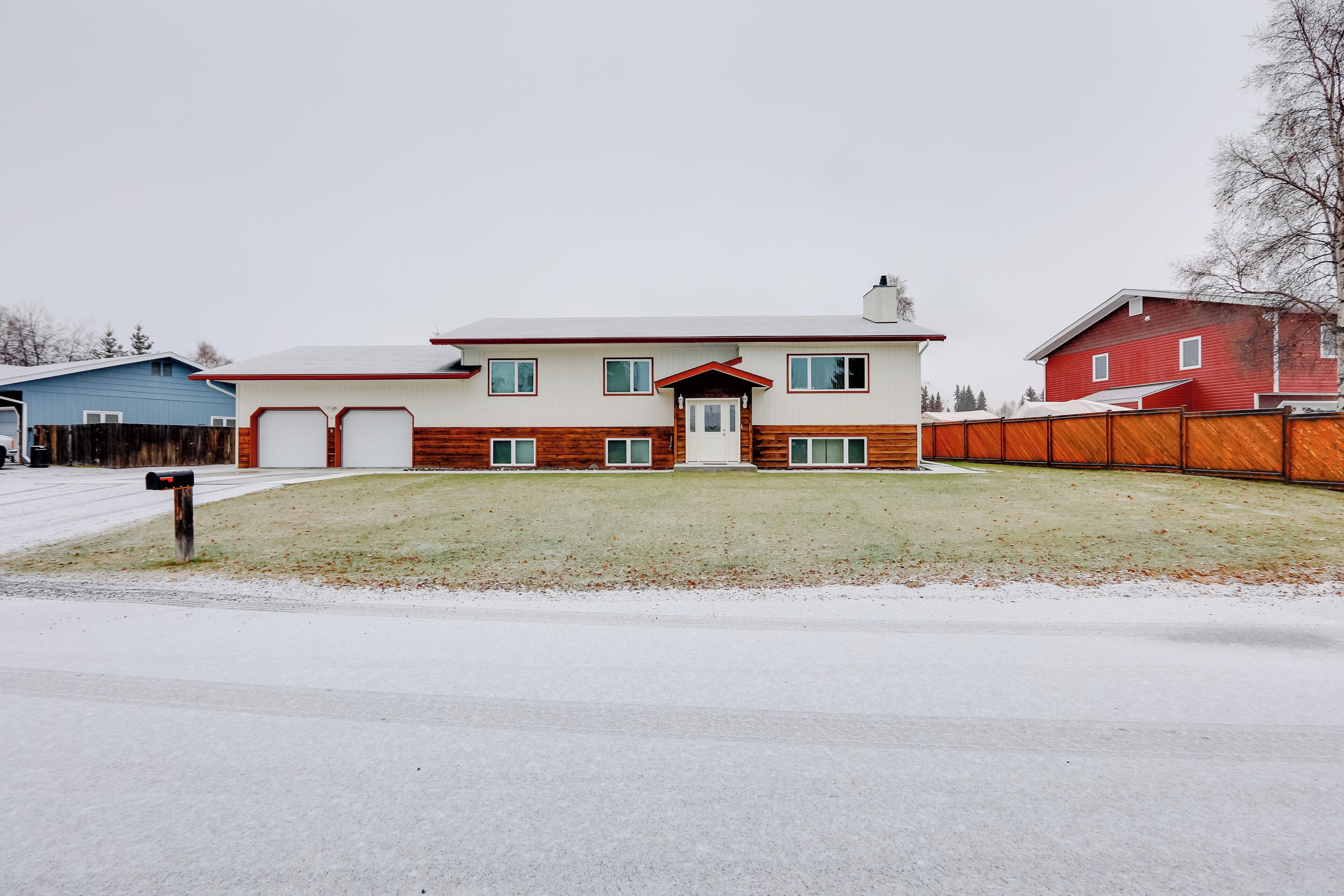 Une maison à deux étages, avec une façade rouge et blanche, un porche à l’avant et une clôture en bois.