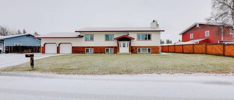 Une maison à deux étages, avec une façade rouge et blanche, un porche à l’avant et une clôture en bois.