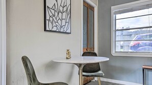 Una habitación con una mesa redonda, dos sillas, un adorno en la pared y una ventana que da a coches aparcados afuera.
