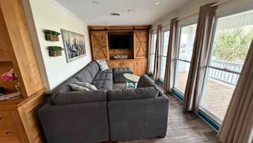 Una sala de estar moderna con un sofá modular, armarios de madera, un televisor de pantalla plana y ventanas grandes.