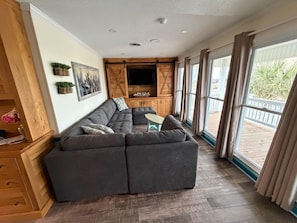A modern living room with a sectional sofa, wooden cabinets, a flat-screen TV, and large windows.