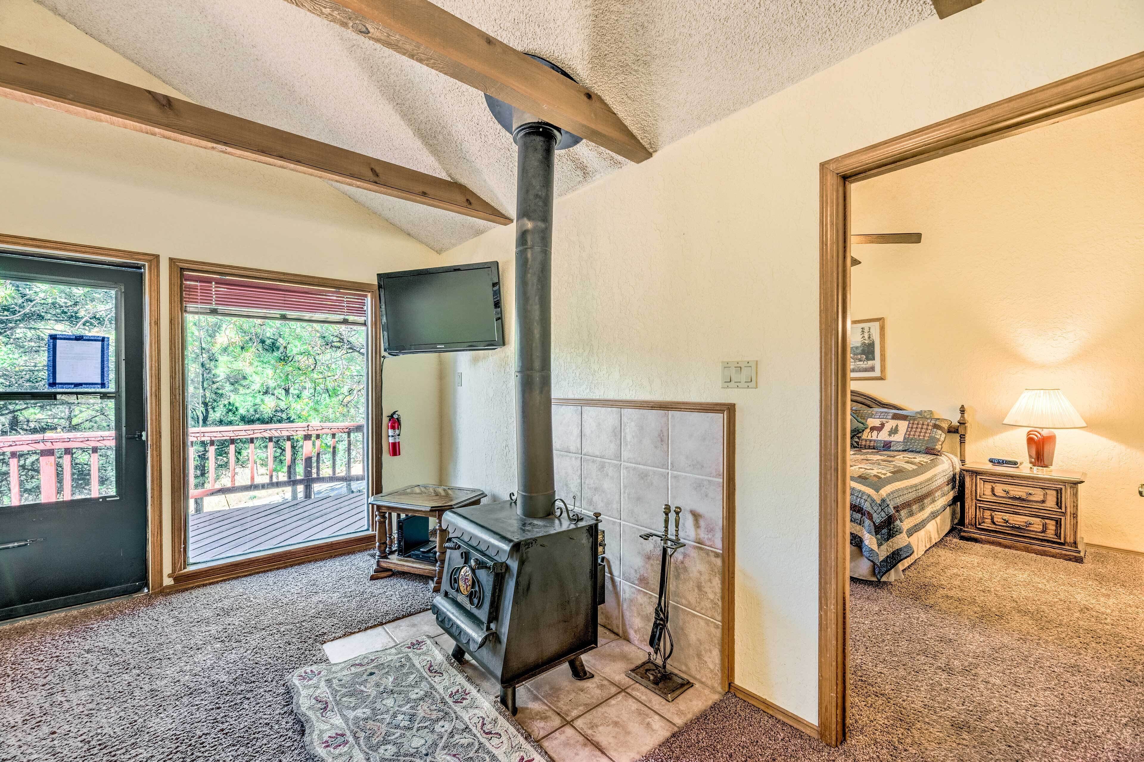A cozy room with a wood-burning stove, a bed with a quilt, a nightstand with a lamp, and a television on the wall.