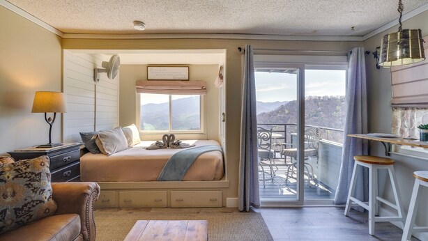 A bedroom with a bed, a desk, a chair, a sofa, and a view of the outdoors.
