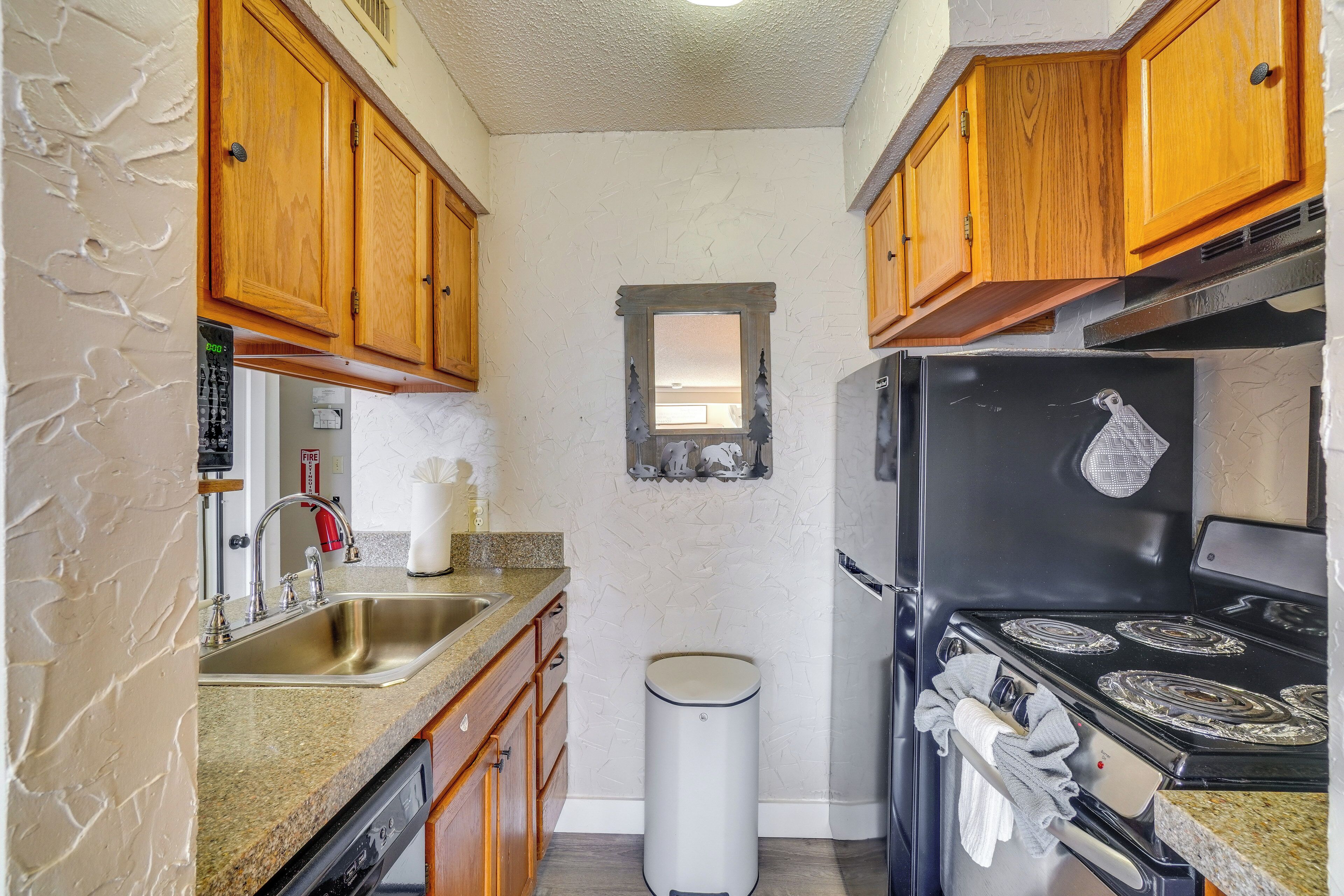 A kitchen with wooden cabinets, a stainless steel sink, a black refrigerator, and a small window.