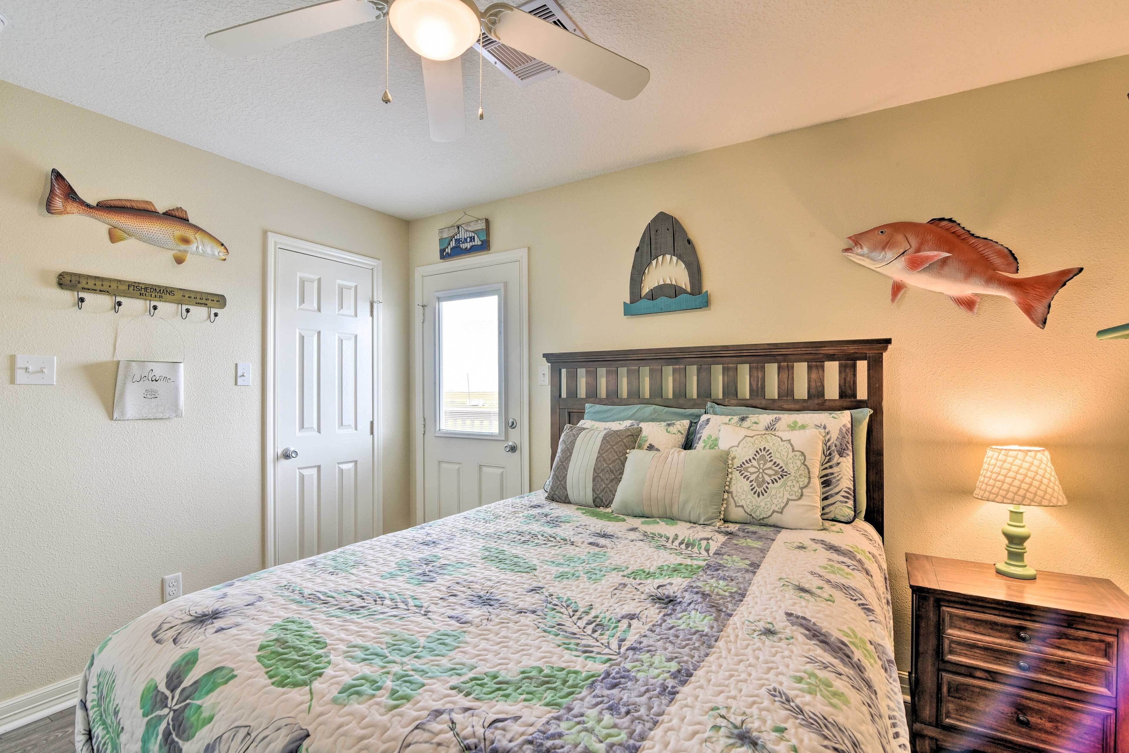 Une chambre à coucher comprenant un lit, une table de chevet, une lampe, un ventilateur de plafond et des éléments de décoration murale, notamment des poissons et une règle.