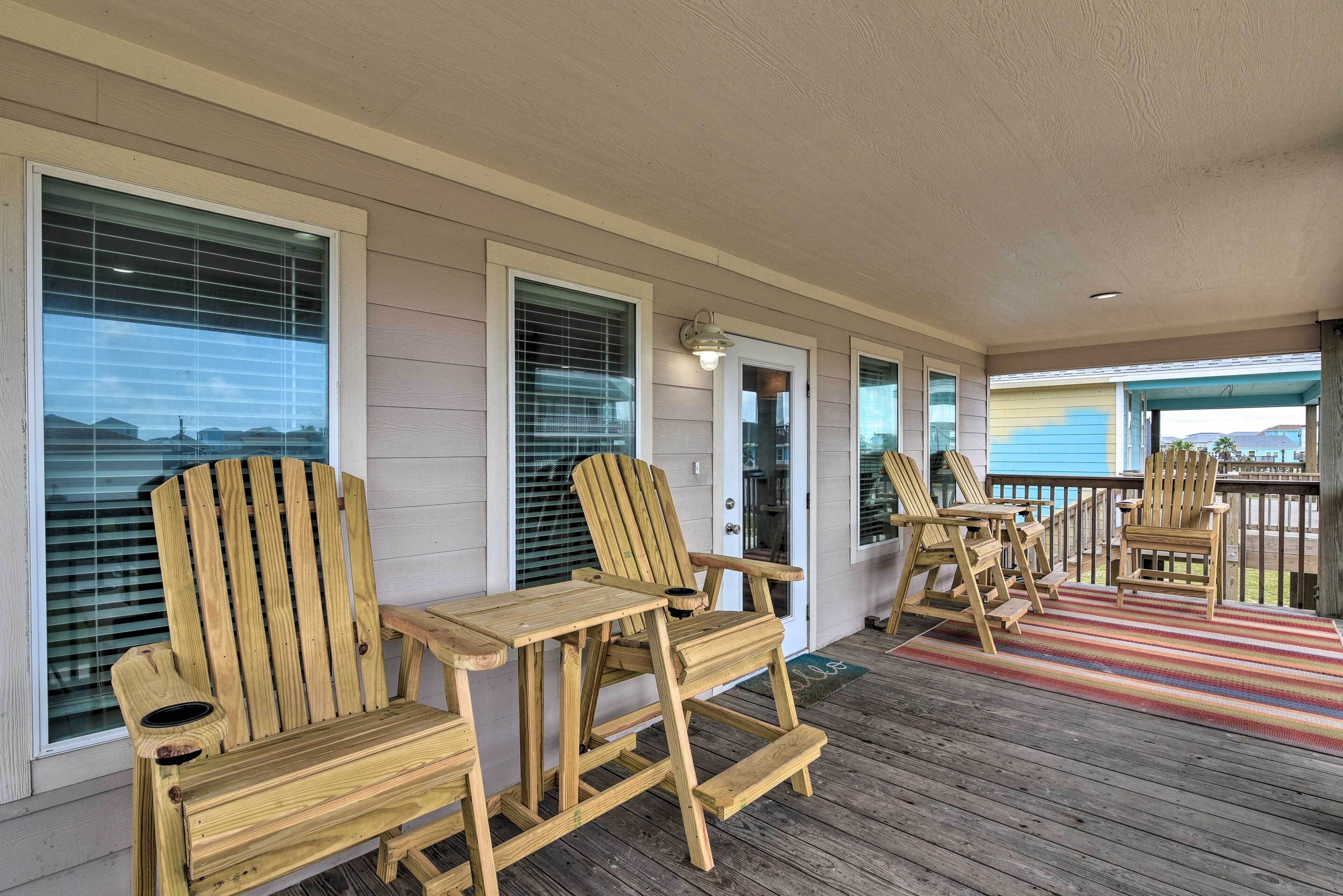 A wooden deck with Adirondack chairs, a small table, and a colorful rug.