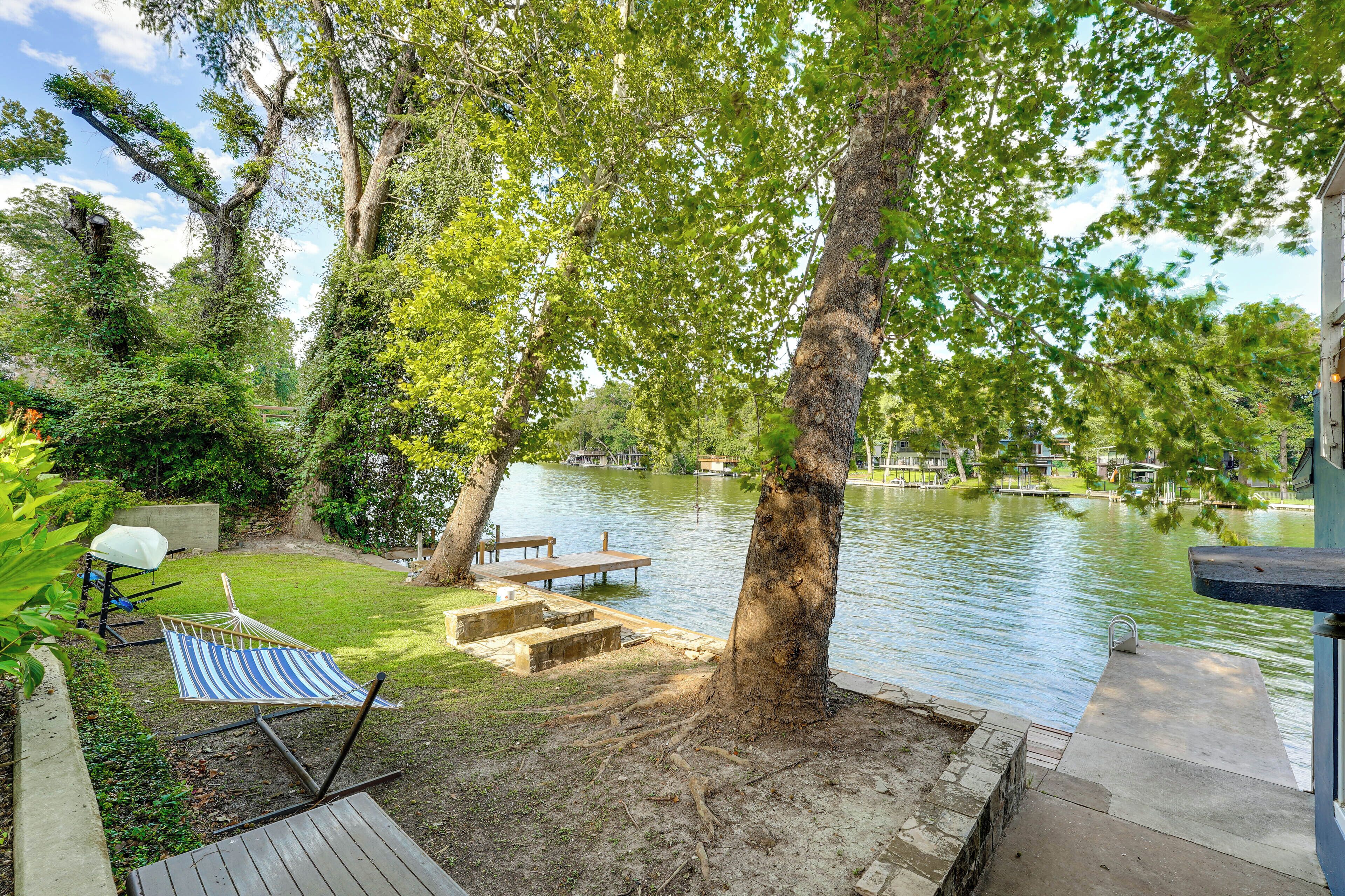 Un patio junto al lago con una hamaca, una mesa de picnic y un muelle que se adentra en el agua.