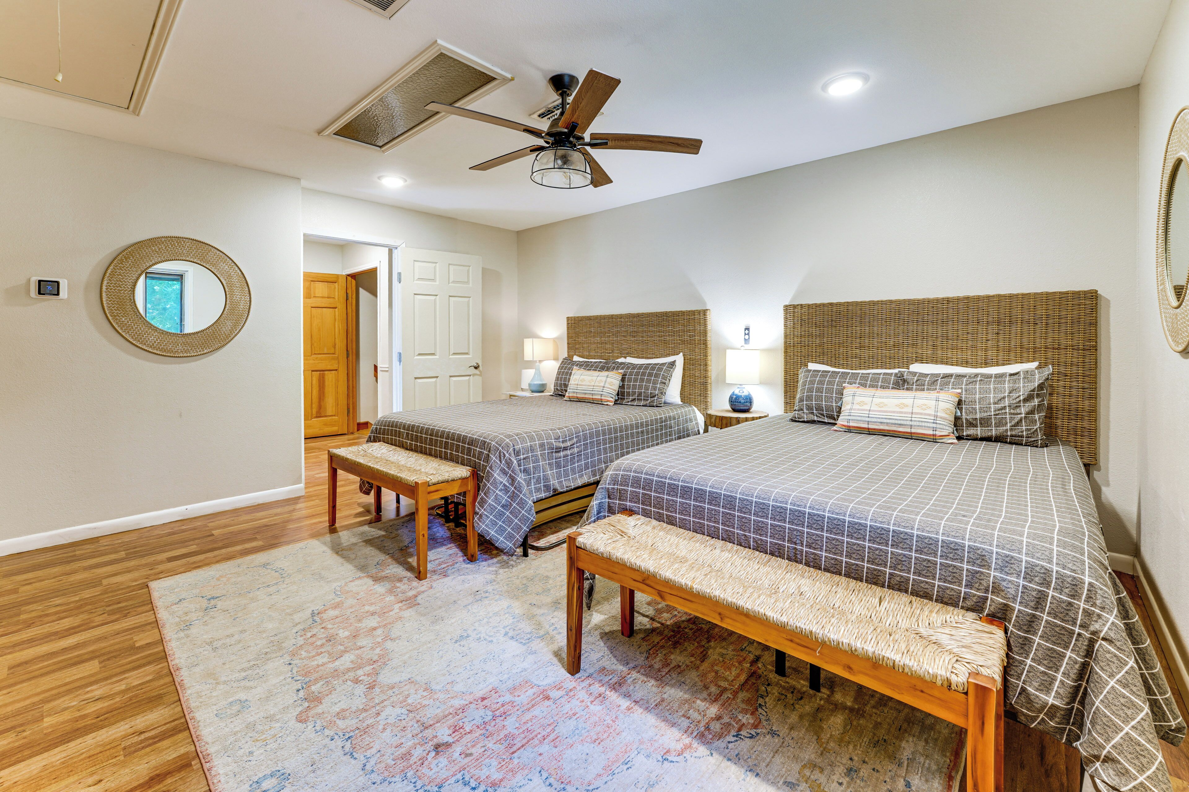 A bedroom with two beds, a ceiling fan, a mirror, and a door.