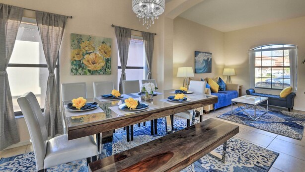A dining area with a wooden table, chairs, and a chandelier. There are flower arrangements on the table, and a sofa and lamp in the background. - Villa w/ Game Room: 10 Mi to Disney! (Davenport)